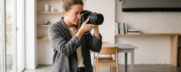 Photographe professionnel cadrant attentivement une prise de vue avec un appareil photo hybride et un objectif premium dans un environnement de shooting lumineux et moderne